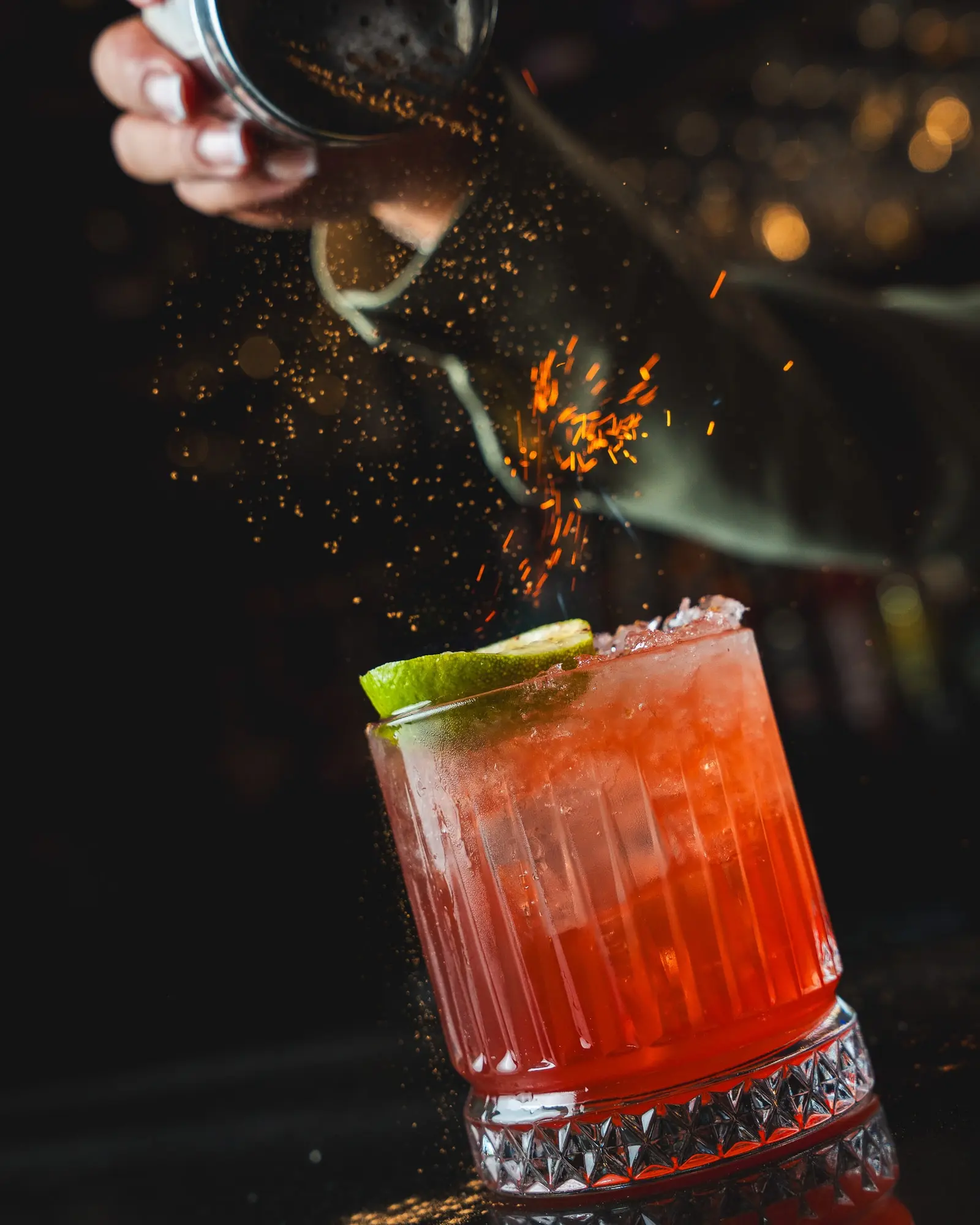 A red cocktail with lime being finished with a shower of glowing sparks.