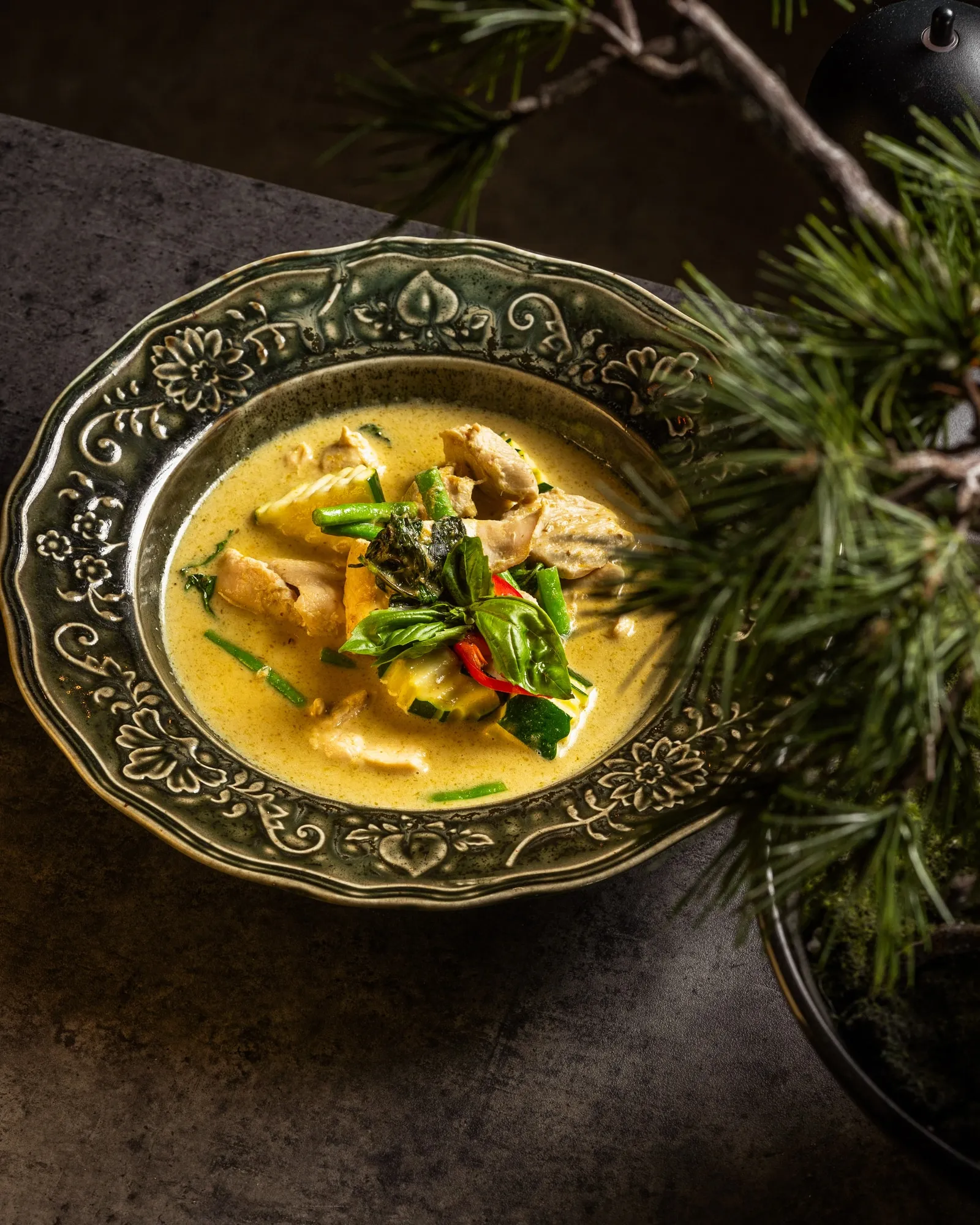 Green curry with chicken, vegetables and fresh basil on a patterned plate.